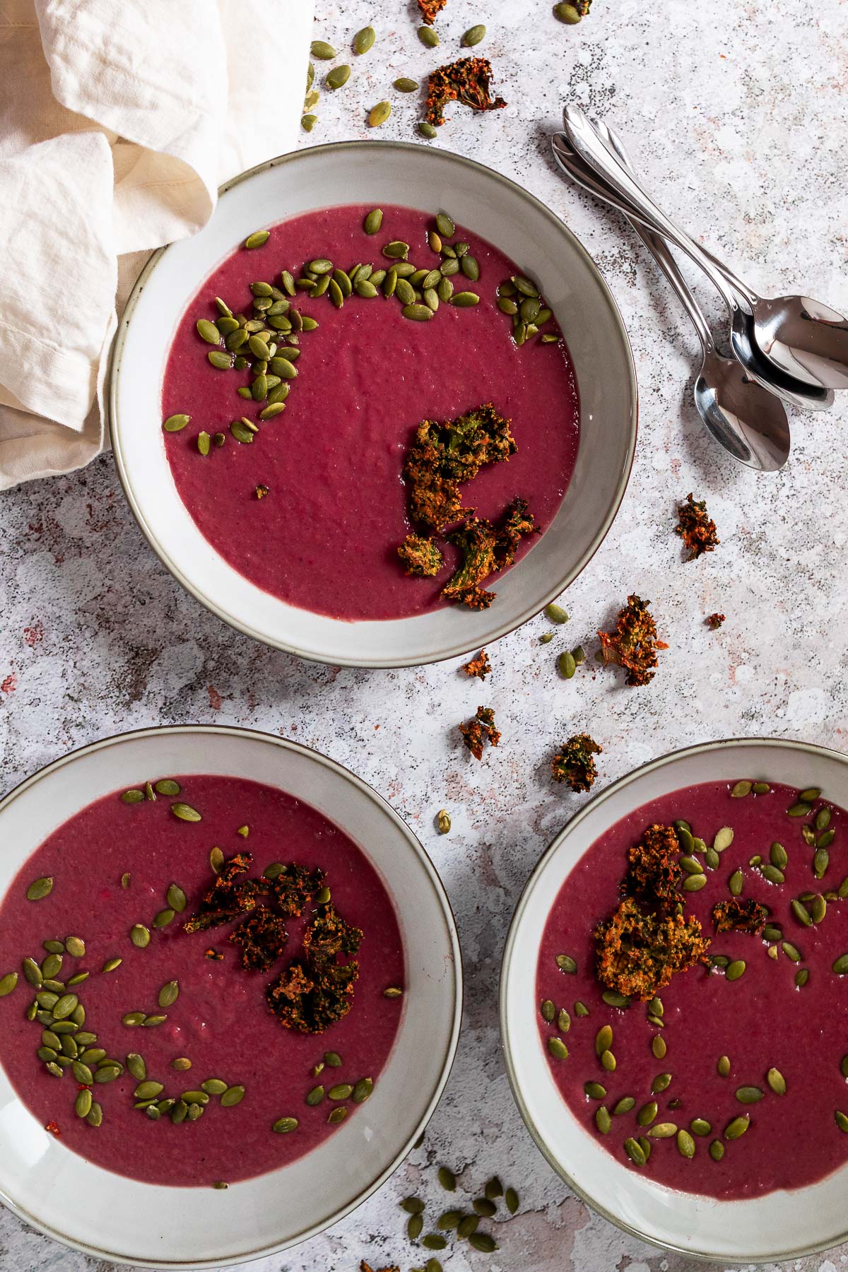 Bird View of 3 plates of vegan red cabbage sooup topped with oil free kale chips and pumpkin seeds.