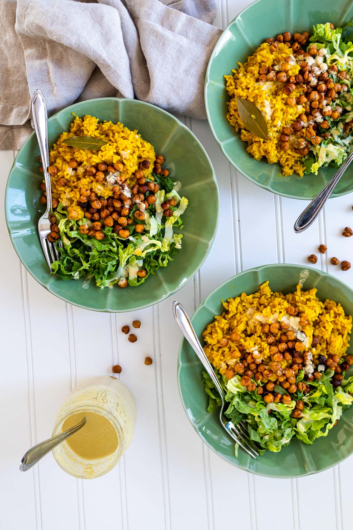 Bird view of three bowls of turmeric rice, lettuce, chickpeas and sauce.