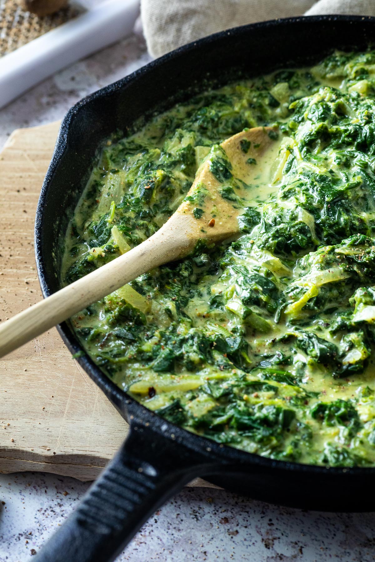 Creamed Spinach in a cast iron pan on a wooden board. A wooden spoon to serve the vegan creamed spinach.