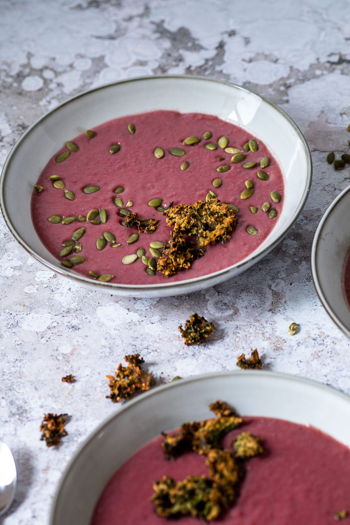 Ein Löffel mit Rotkohlsuppe über einer Schüssel mit veganer Rotkohlsuppe mit zwei Schalen hinten.