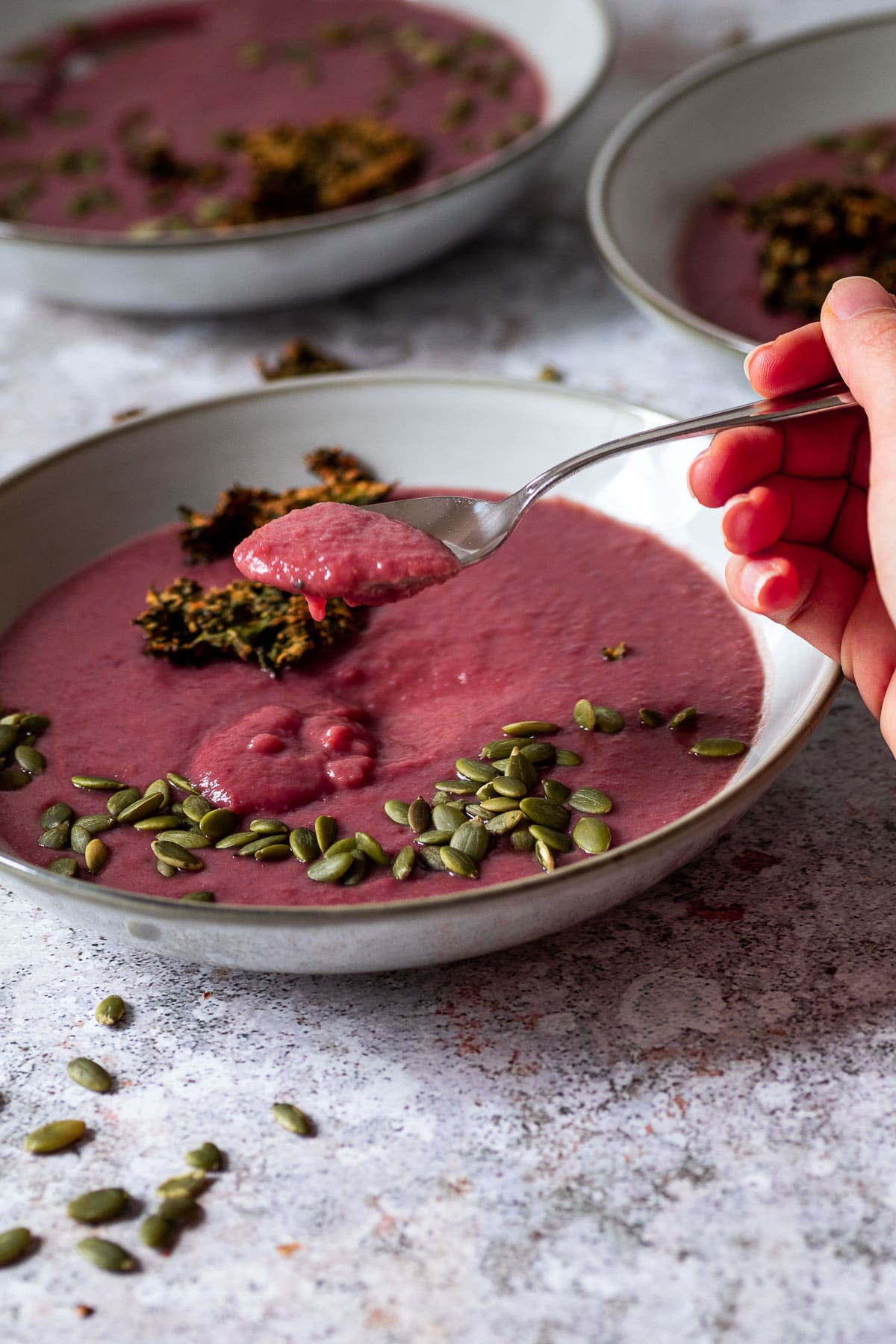 A spoon with red cabbage soup over a bowl with vegan red cabbage soup with two bowls in the back.