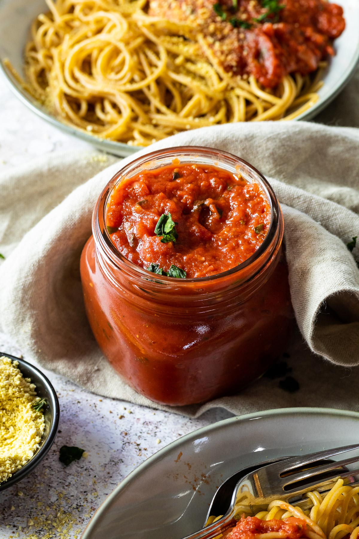 A jar with marinara sauce with a bowl with pasta and sauce in the back as well as in the front