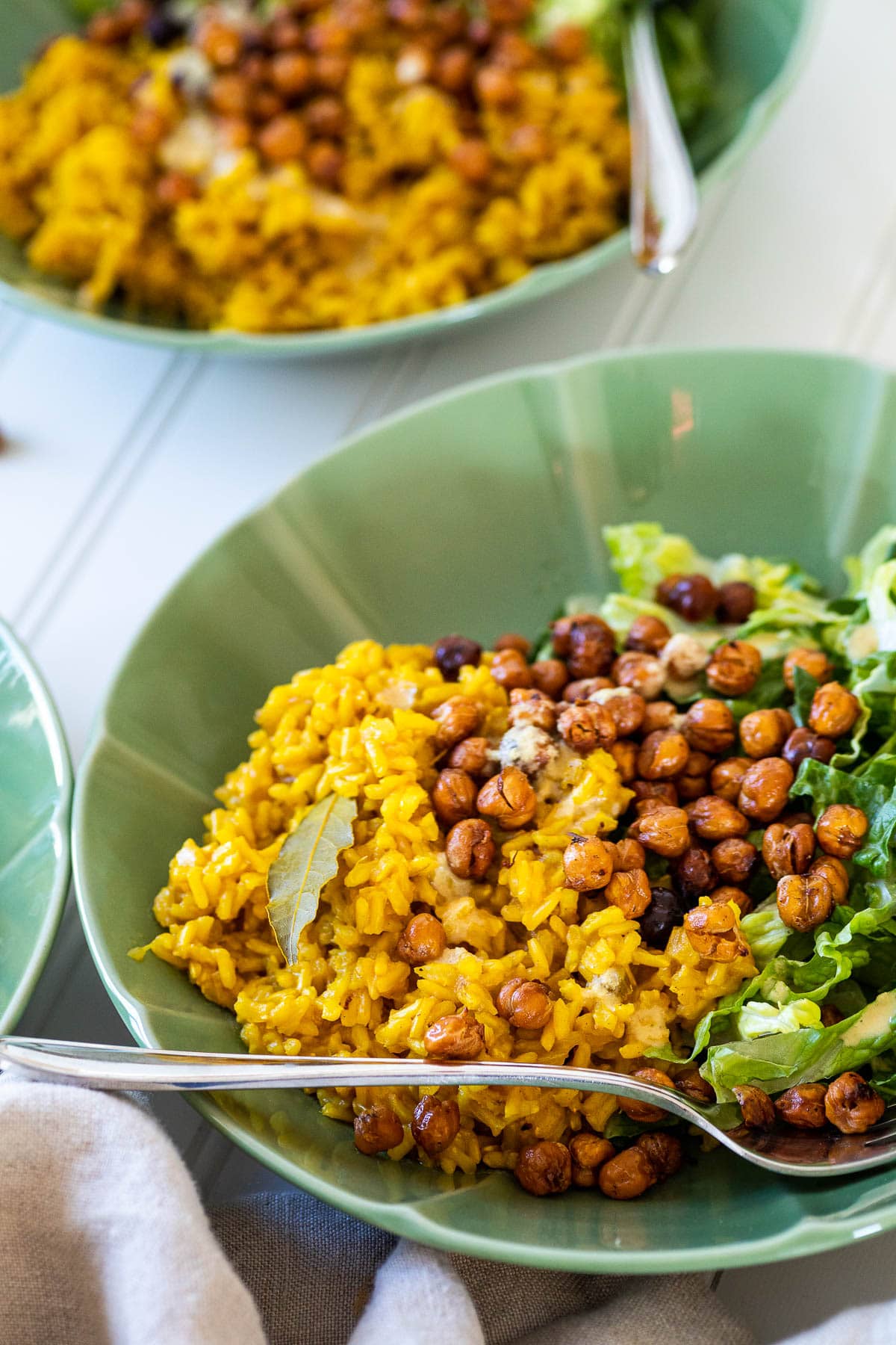 Eine Schüssel mit Kurkuma-Reis, Salat und knusprigen Kichererbsen vor einer anderen Schüssel.