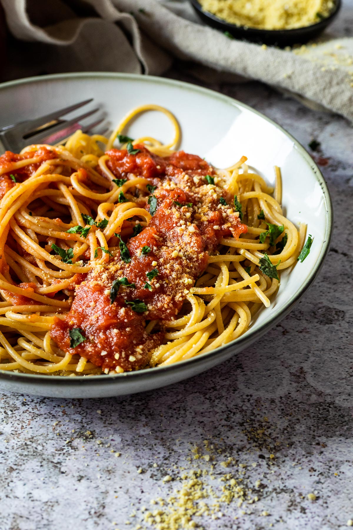 A jar with marinara sauce with a bowl with pasta and sauce in the back as well as in the front