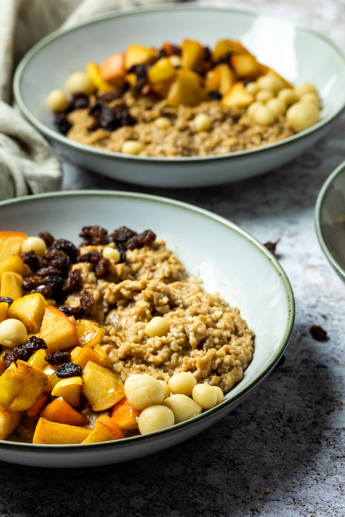 In focus one bowl with oatmeal baked apple and one in the background blurred