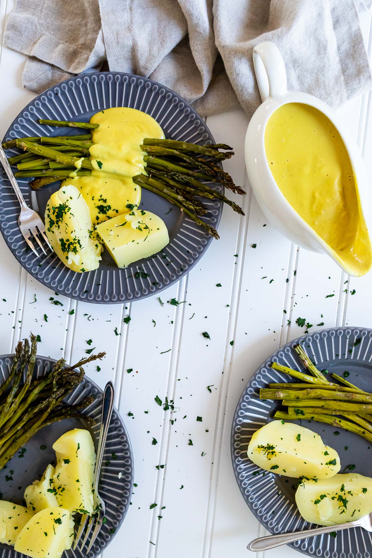 3 plates with asparagus, potatoes and vegan hollandaise sauce and one saucier with hollandaise