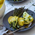 Ein Teller mit Kartoffeln, Spargel und milchfreier Sauce Hollandaise mit einem Teller im Hintergrund