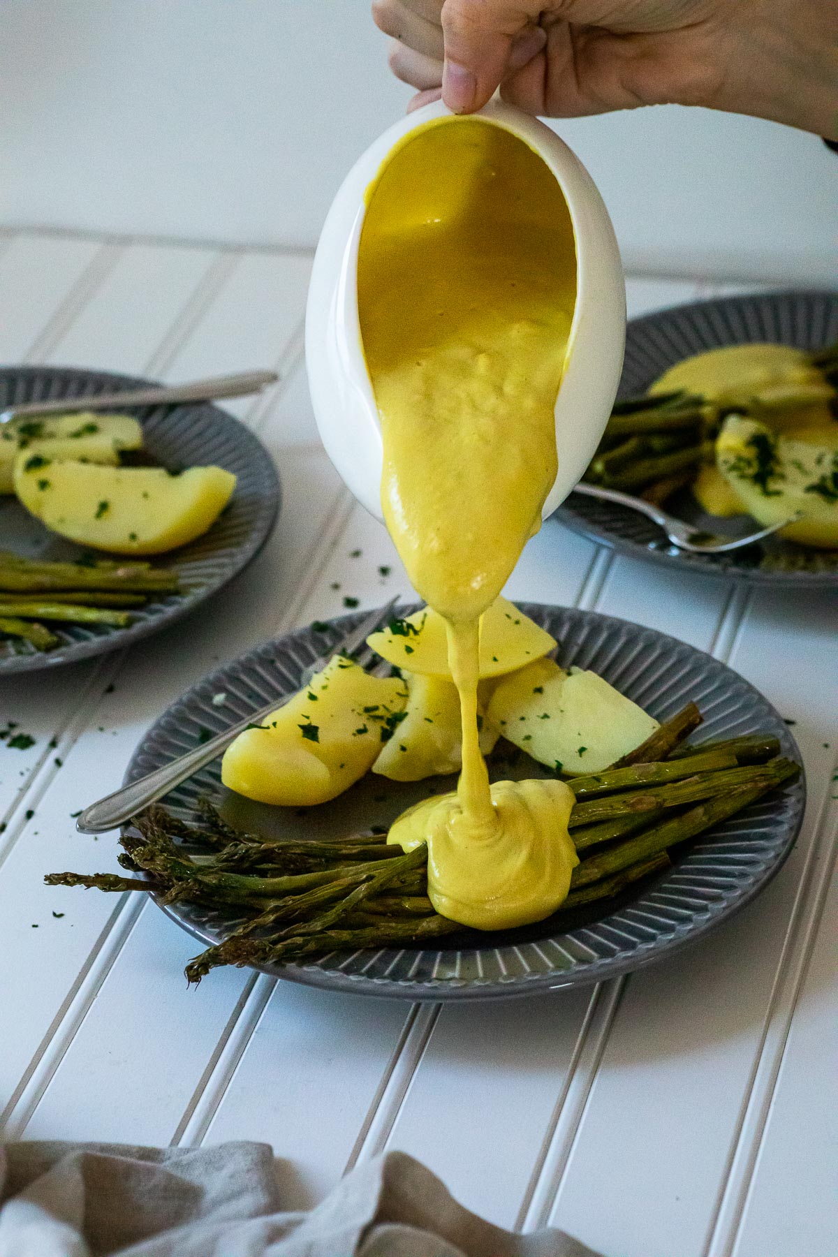 Gieße etwas vegane Sauce Hollandaise auf einen Teller mit Spargel und Kartoffeln