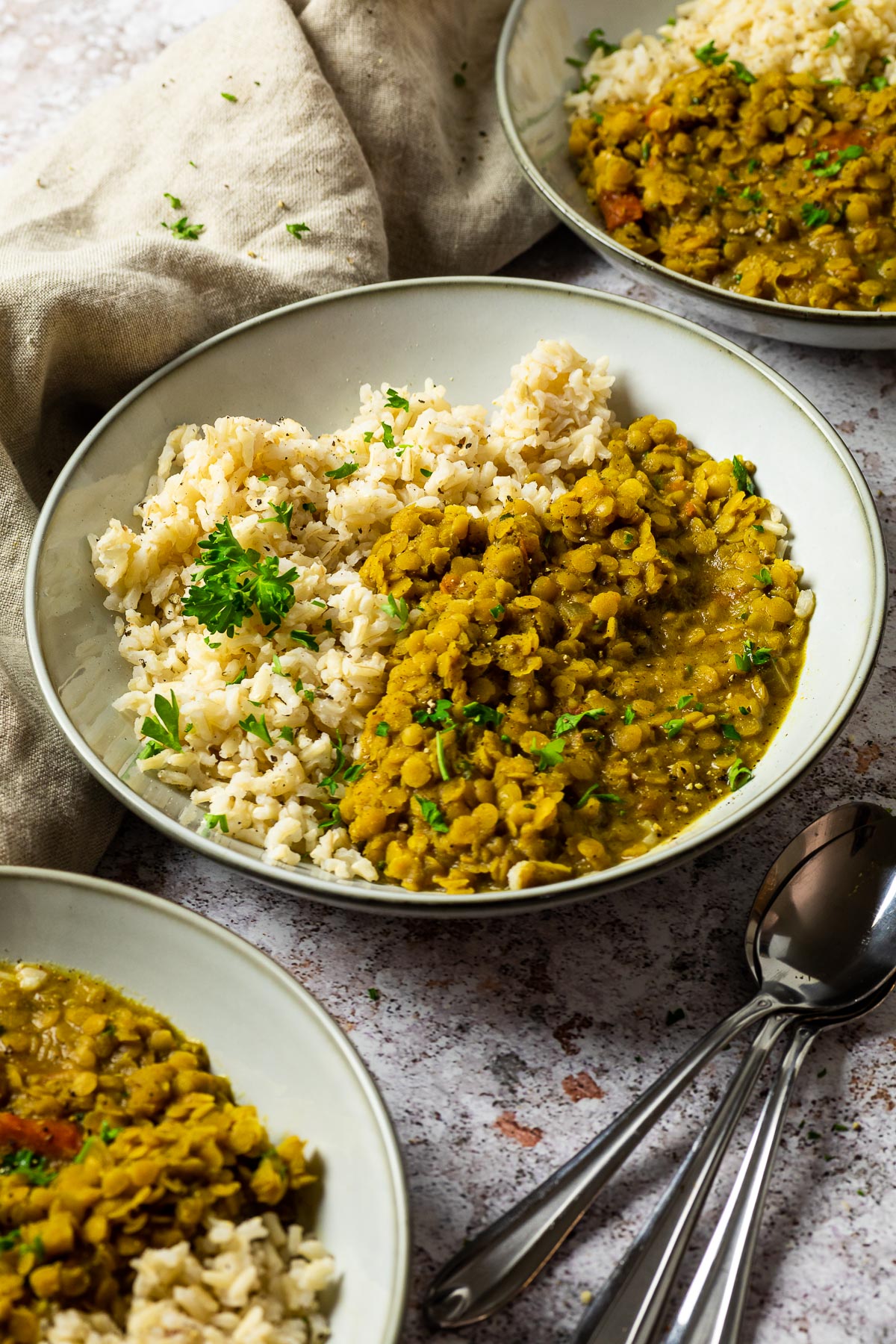 Eine Schüssel mit veganem rotem Linsen-Dal und braunem Reis im Fokus, eine vorne und eine hinten