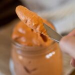 Nahaufnahme des Russian Dressing auf dem Messer mit dem Glas Russian Dressing im Hintergrund verschwommen