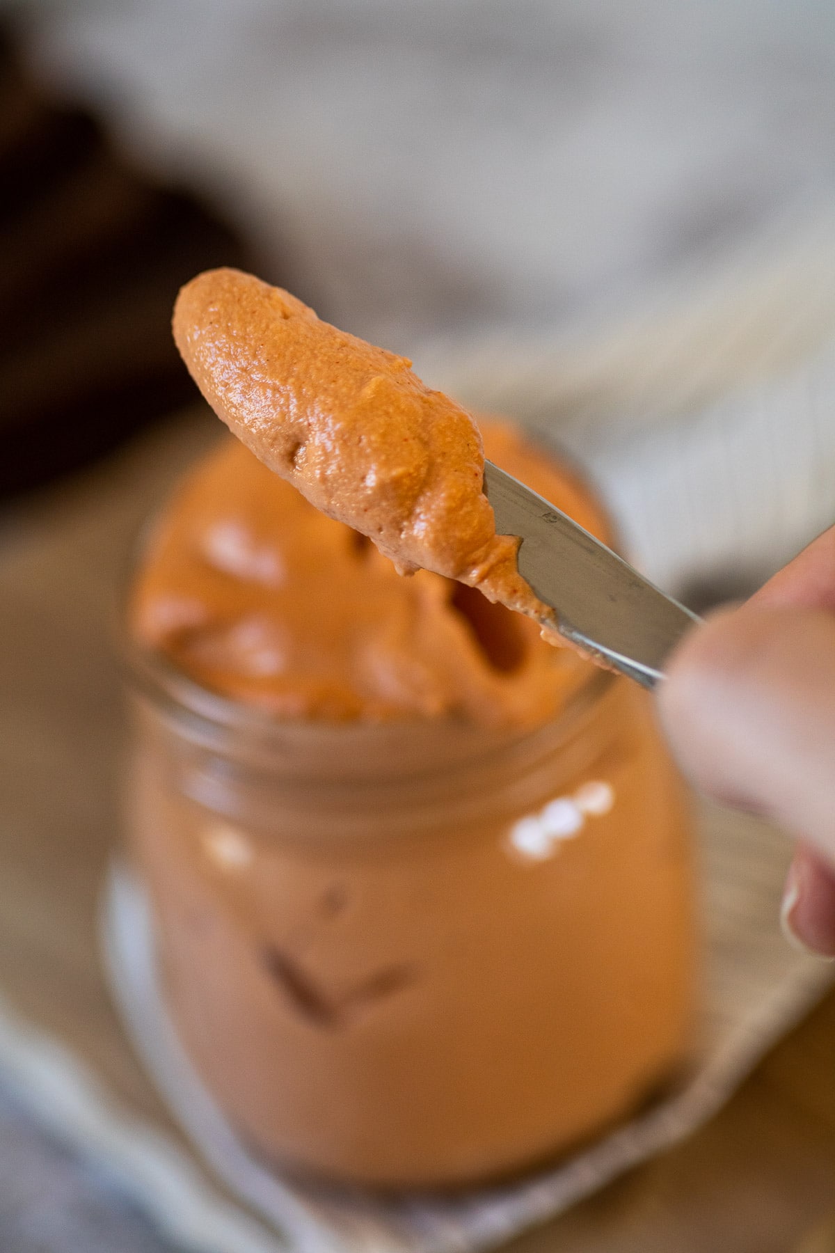 Close up of Russian dressing on the knife with the glass of Russian dressing blurred in the background