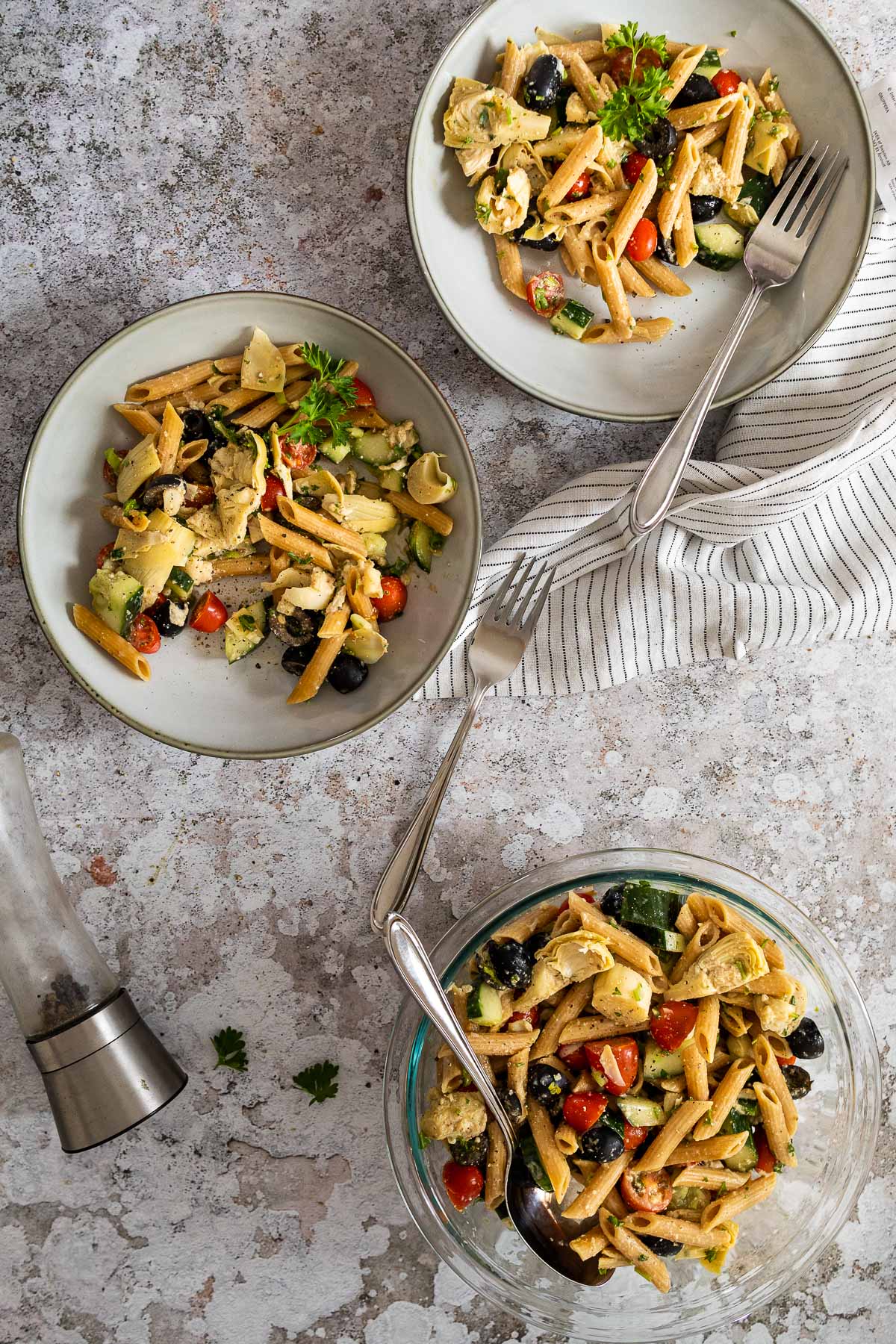 Bird view of two salad bowls with pasta salad and a serving bowl with artichoke pasta salad