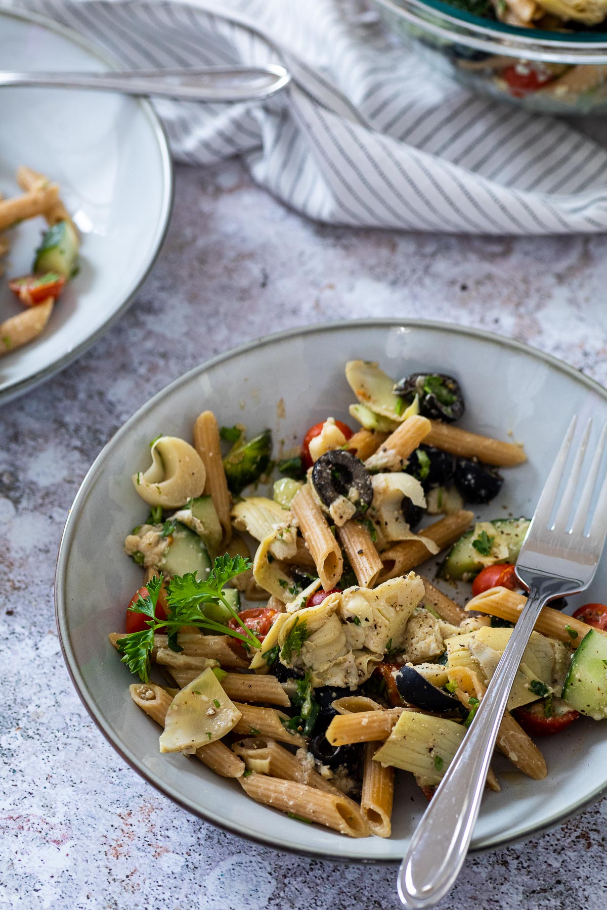 A salad bowl with pasta salad and the serving bowl in the background