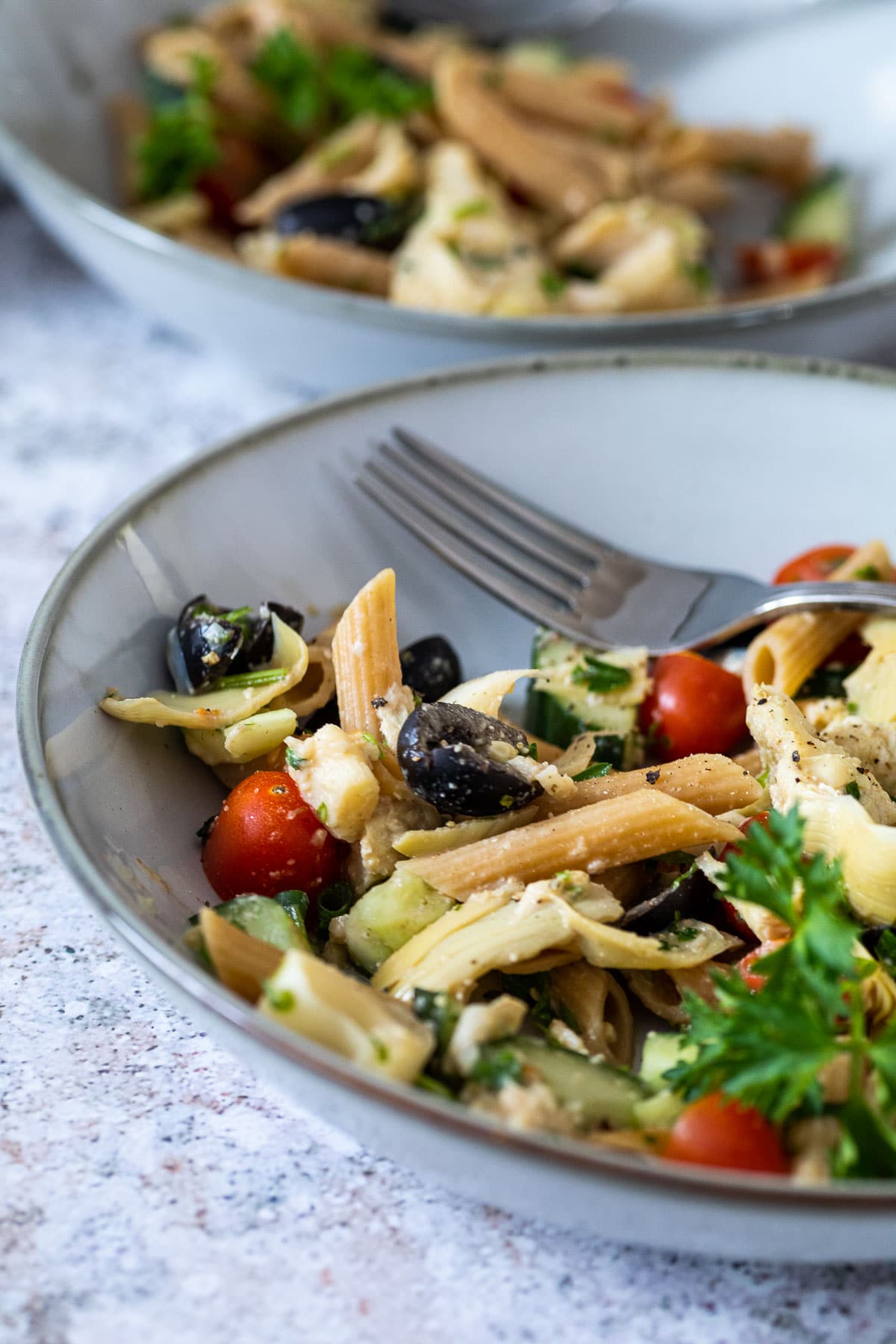 a plate with vegan artichoke pasta salad with a plate in the background