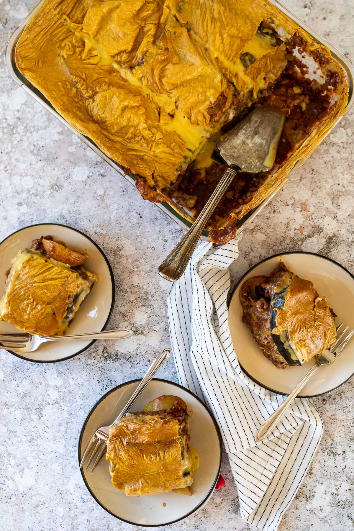 Bird view of 3 plates with a piece of vegan moussaka and the casserole pan