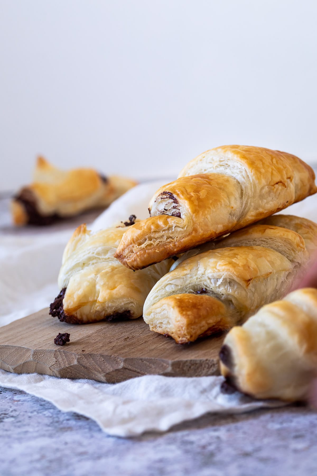 Flaky chocolate croissants on a wooden board with a croissant blurred in the backgroound