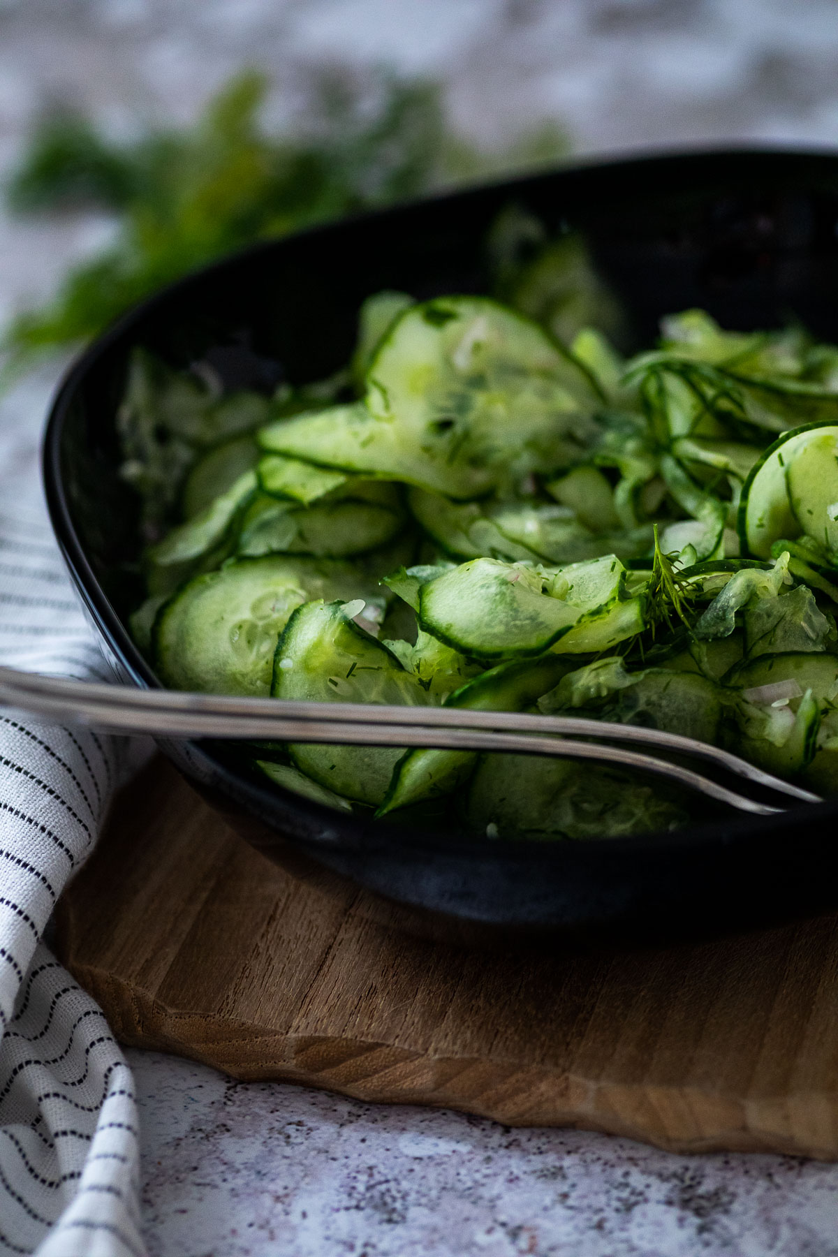 A cucumber bowl on a wooden board with some dill in the background