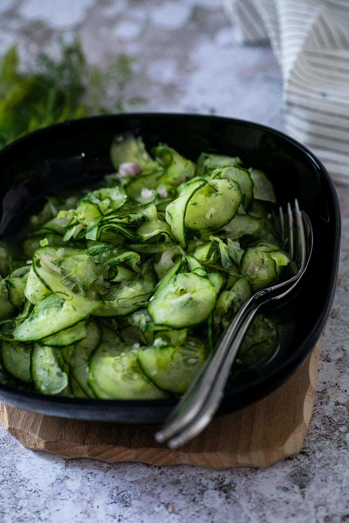 A bowl with cucumber salad with a fork and a spoon in the bowl