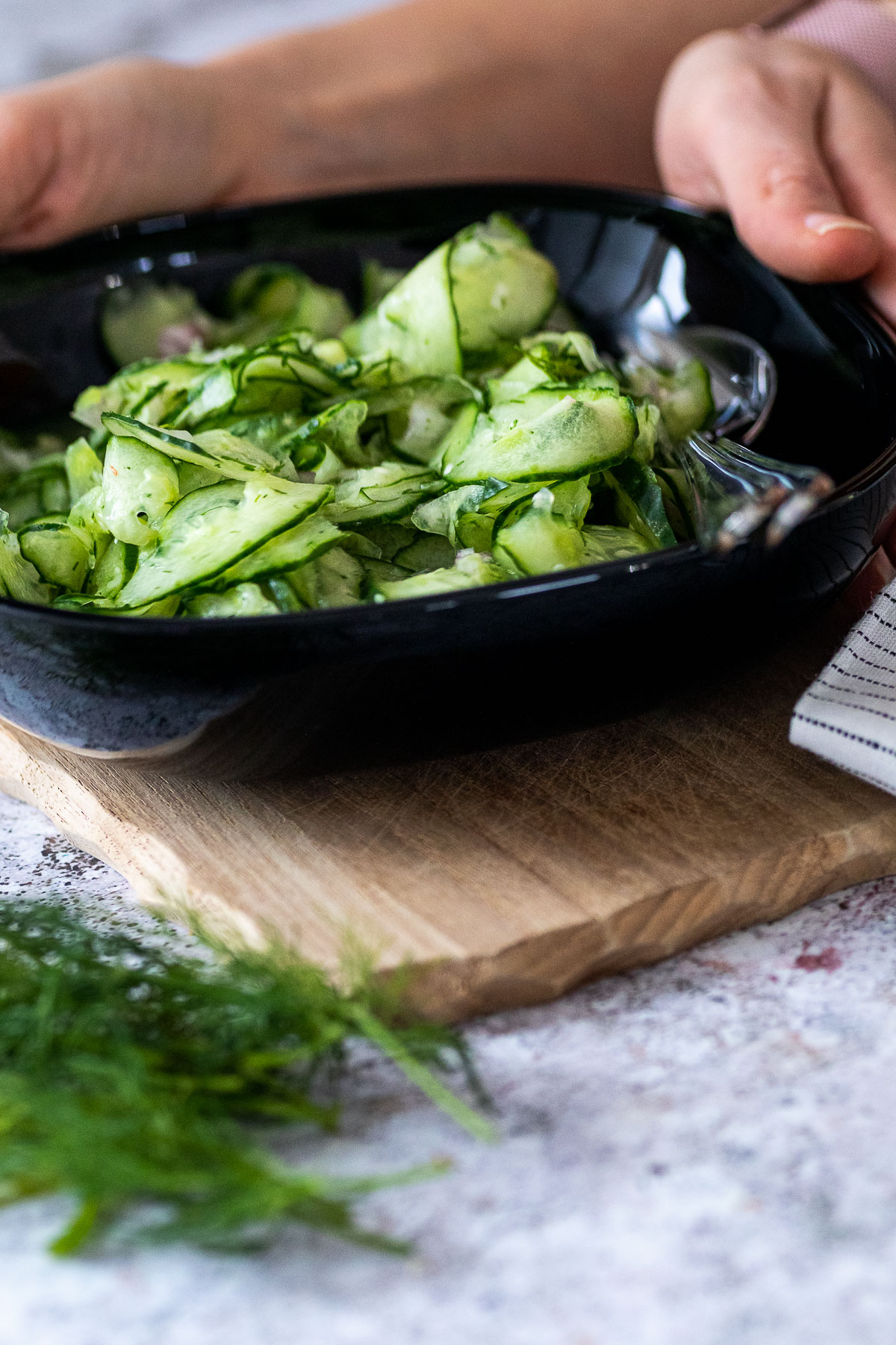 Holding a bowl with cucumber salad with some dill in the front blurred