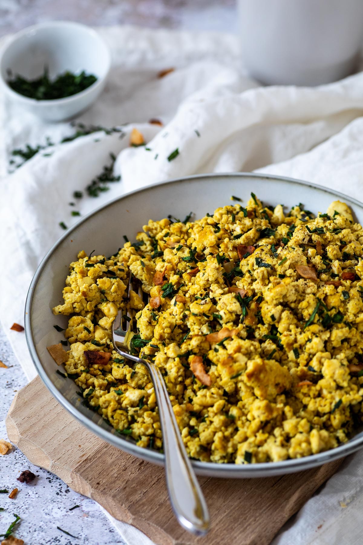 A bowl with scrambled tofu sprinkled with coconut bacon and parsley