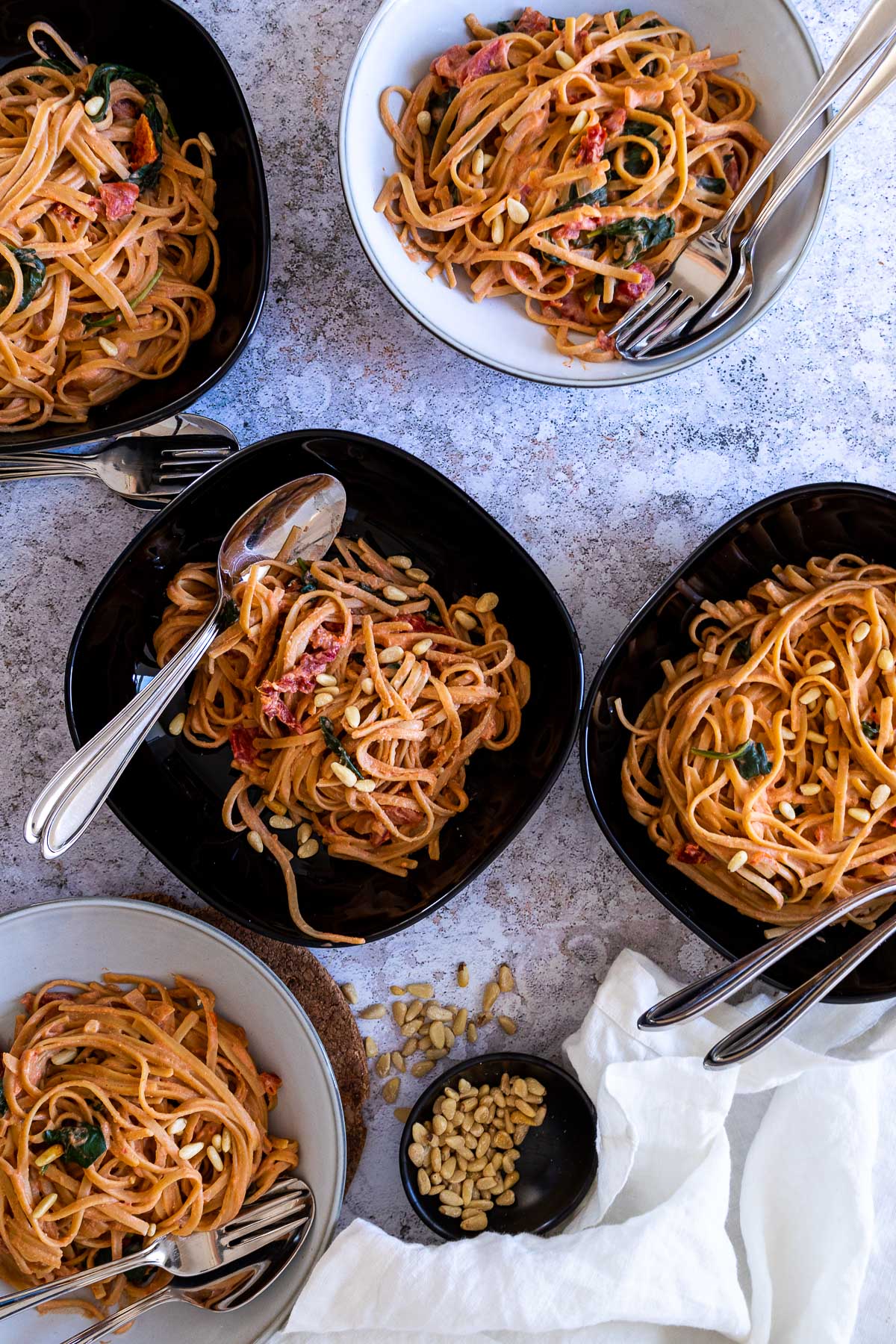 Five bowls with tomato alfredo spaghetti topped with pine nuts