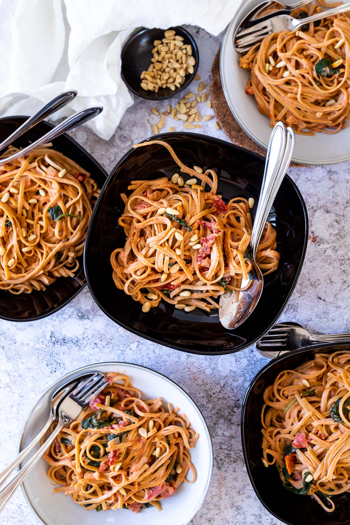 Vegan Tomato Alfredo Spaghetti served in bowls . 3 black bowls and 2 white bowls