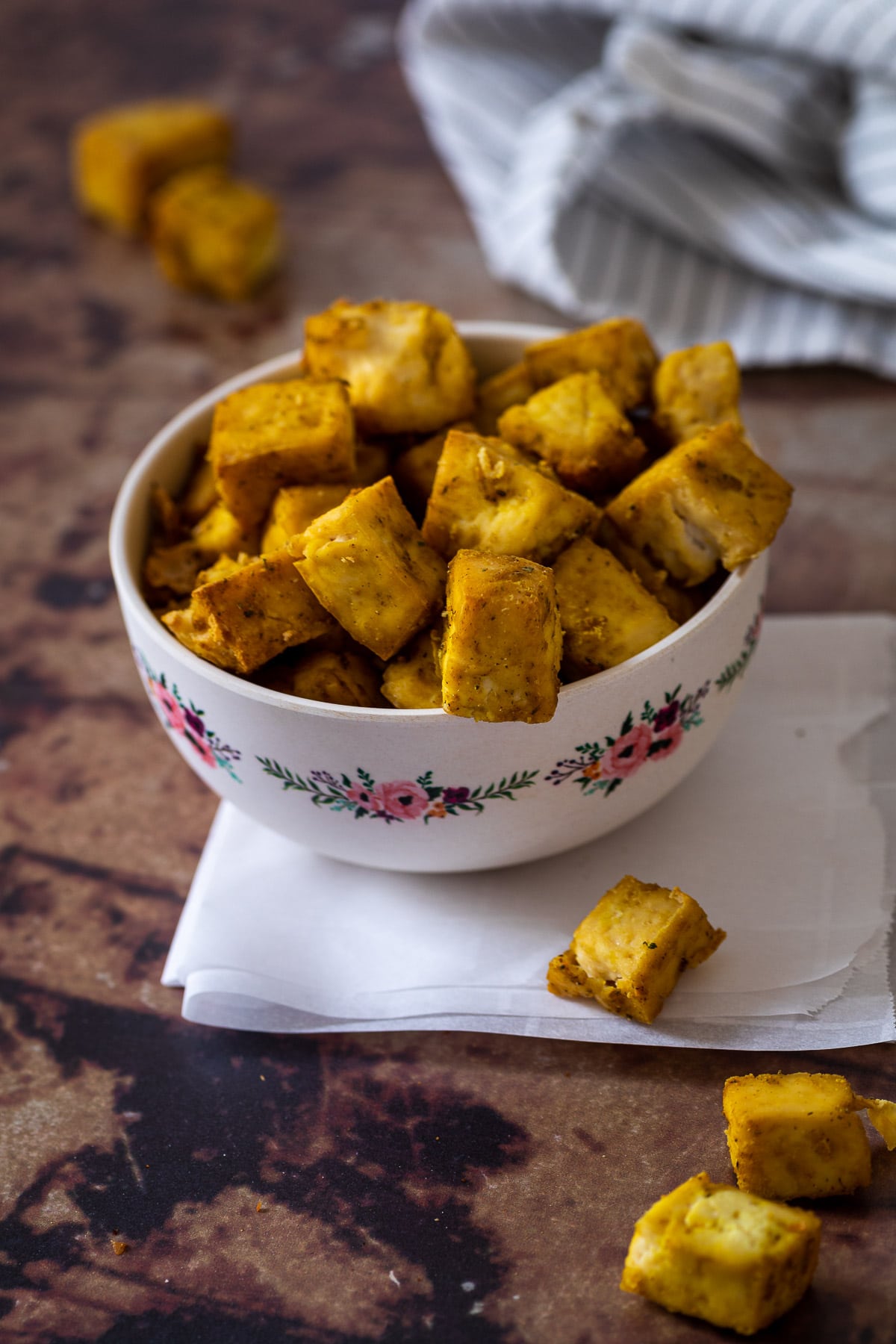 Small bowl filled with crispy baked chicken tofu nuggets on parchment paper