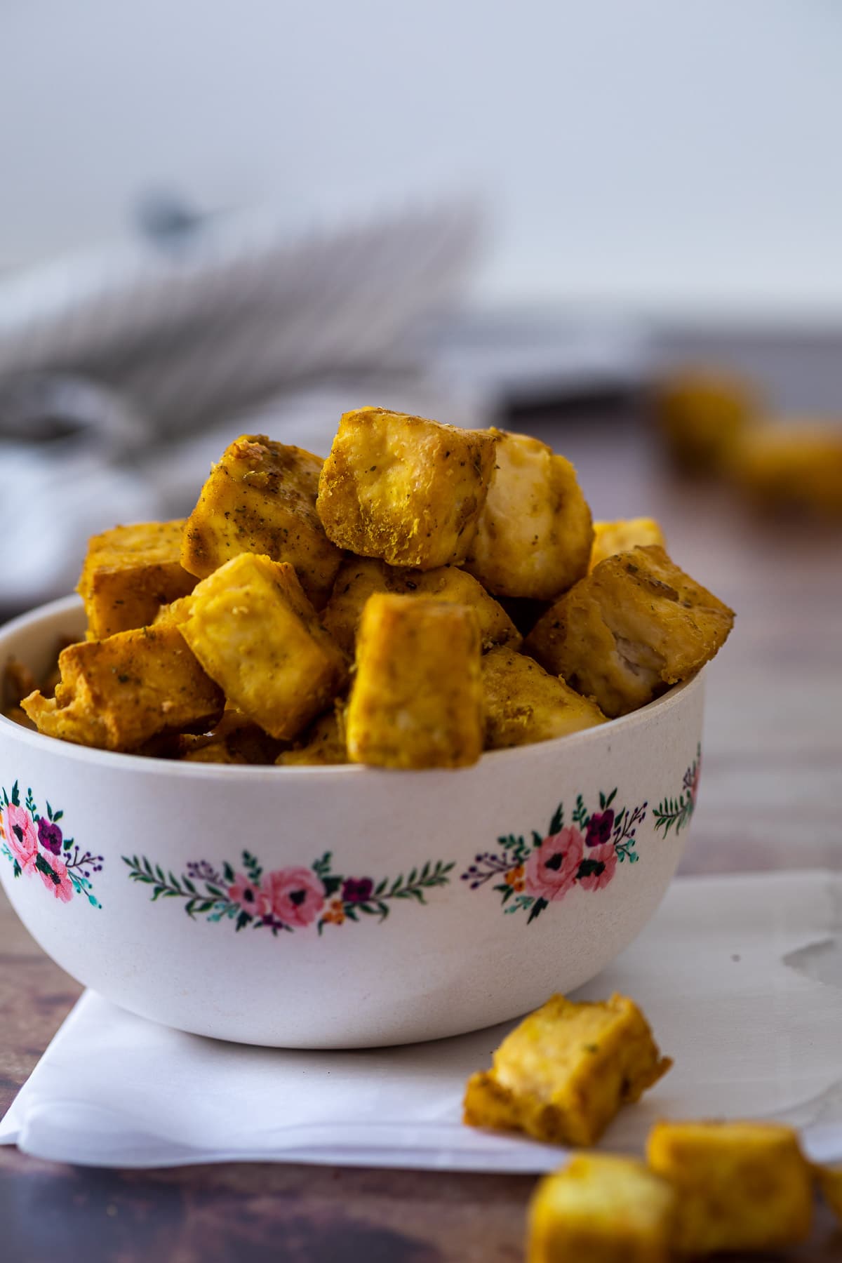 Close up of a bowl filled with cubed chicken style tofu bites and some a laying in front of the bowl.