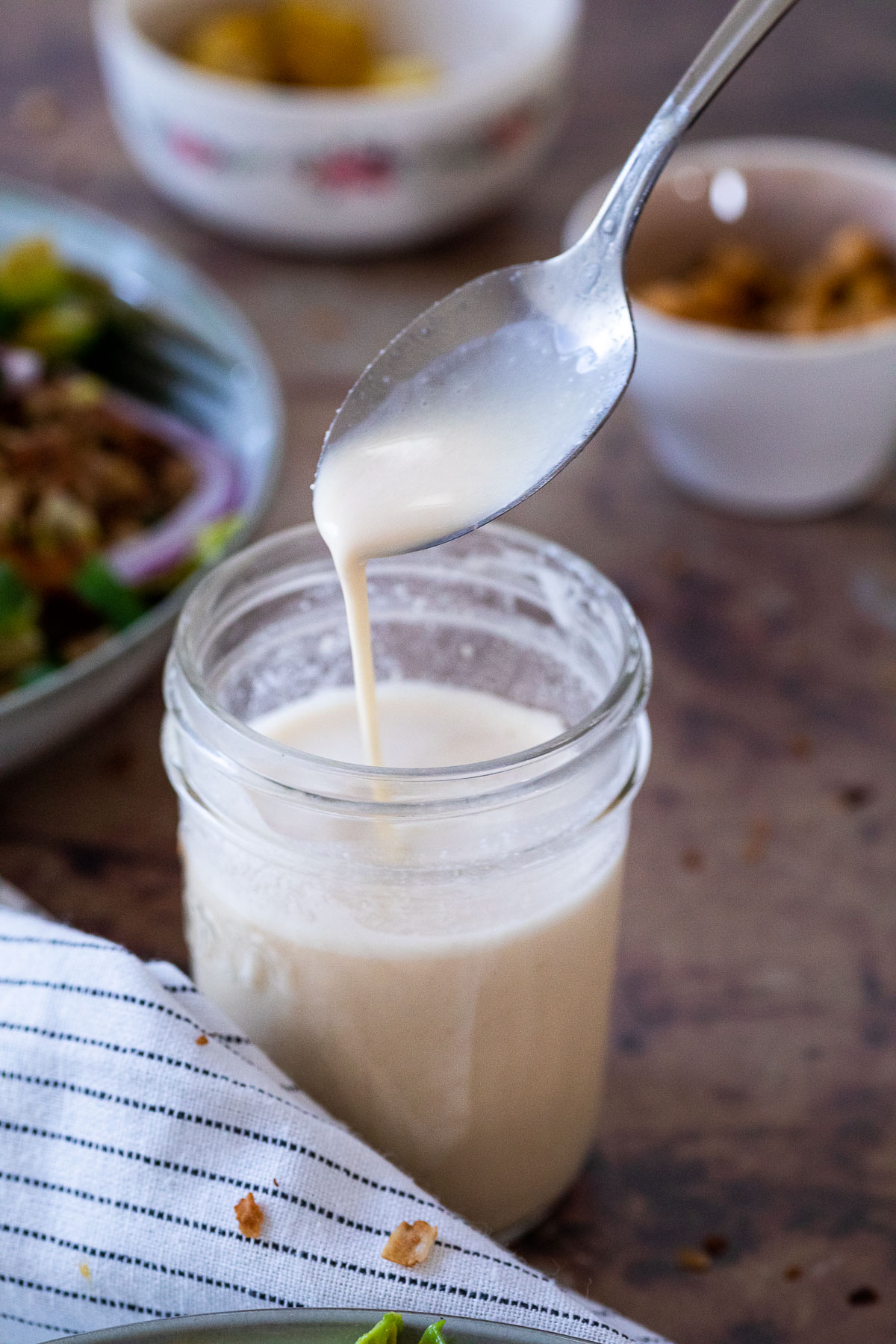 Spoon over a mason jar. Some tahini dressing is dripping from the spoon in the jar.