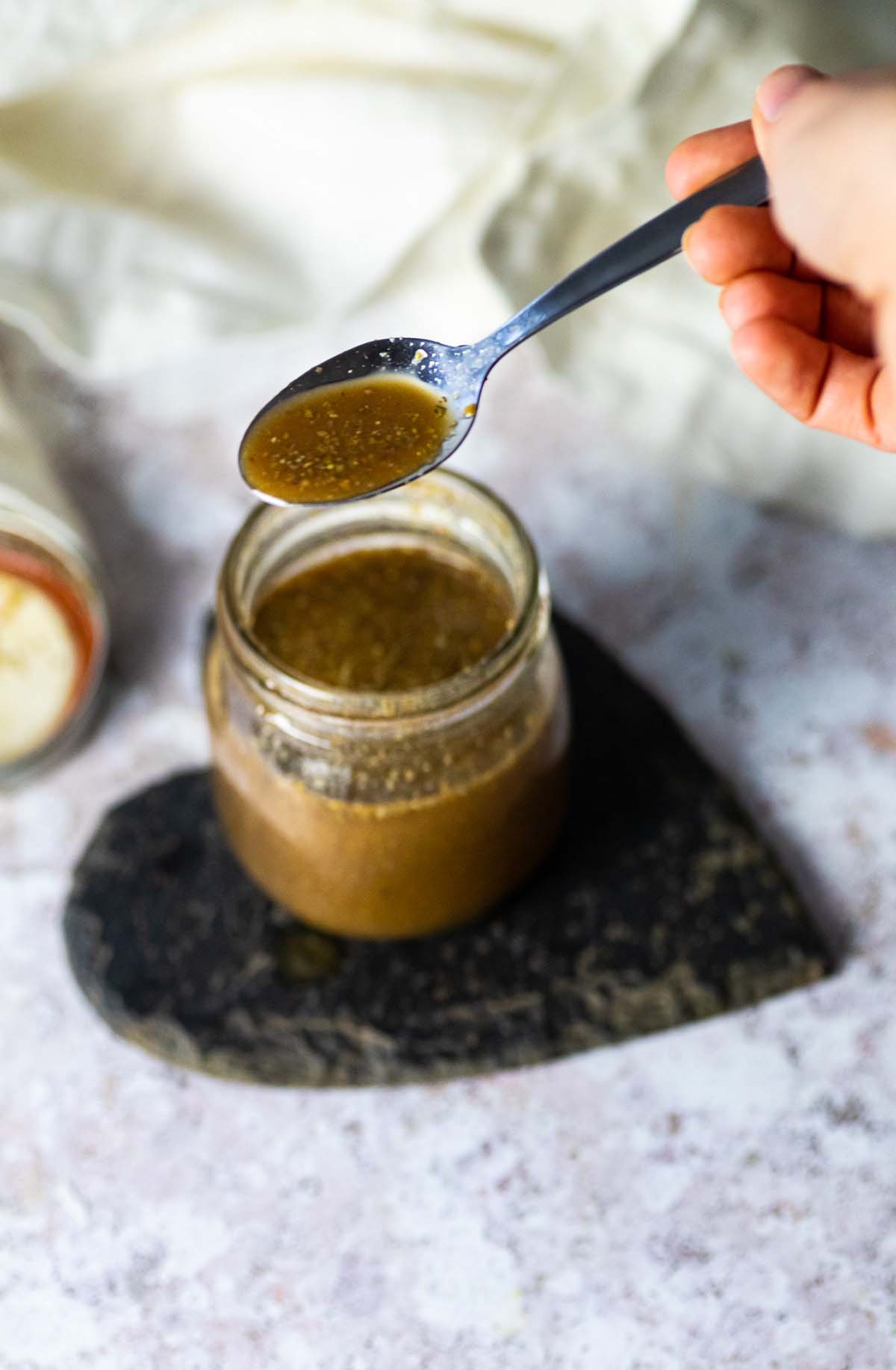 Holding a spoon with oil free balsamic dressing over a balsamic vinaigrette jar