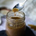 Some balsamic dressing is dripping from a spoon into a jar.