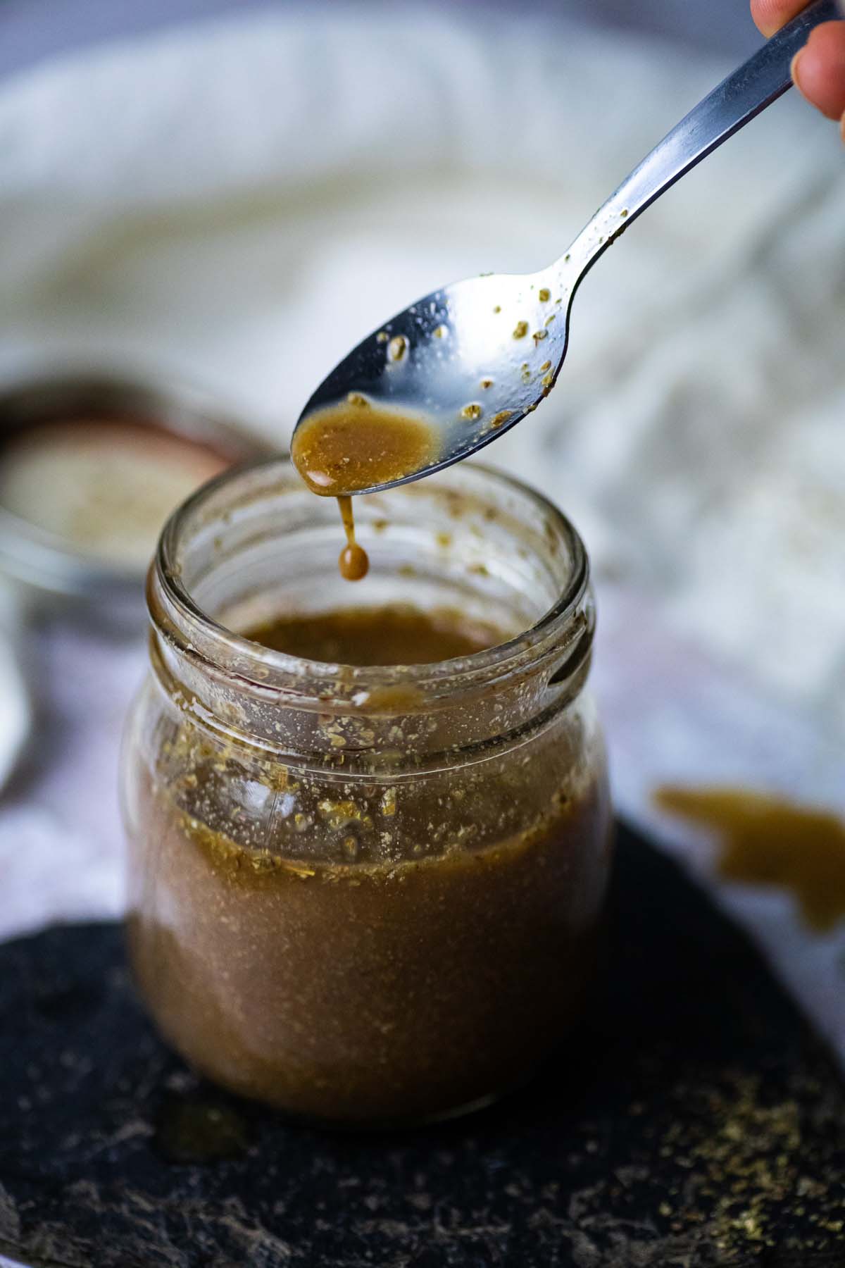 Etwas Balsamico-Dressing tropft von einem Löffel in ein Glas.