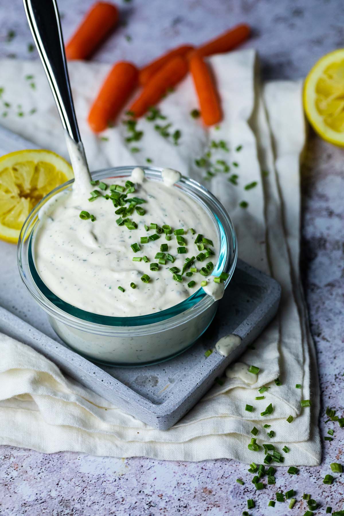 A bowl of ranch with a spoon in it on some cloth and board.