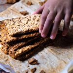Close up of a stack seed crackers with a child hand reaching for it.