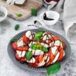 vegan tomato mozzarella salad on a plate with fresh basil leaves on top.
