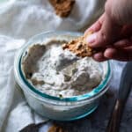 Holding a cracker dipped in the vegan olive cream cheese over the bowl with cream cheese.